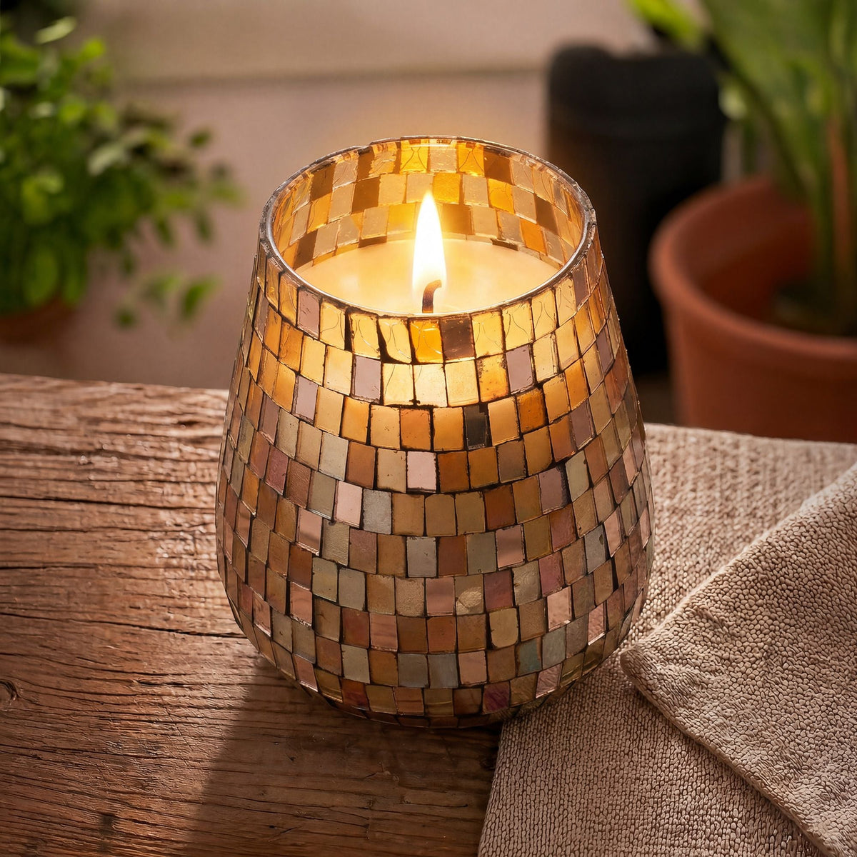 A lit amber mosaic glass candle on a rustic wooden table with linen