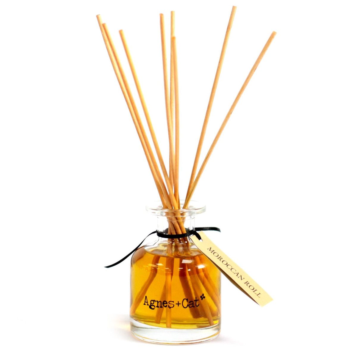 An amber reed diffuser bottle with natural reeds on a white background