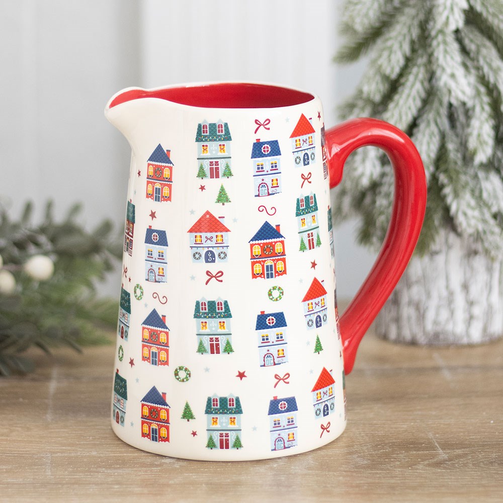 Cream ceramic jug with a red handle, printed with rows of small Christmas houses and trees