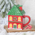 Ceramic mug shaped like a red Christmas house with a green roof lid and lit windows