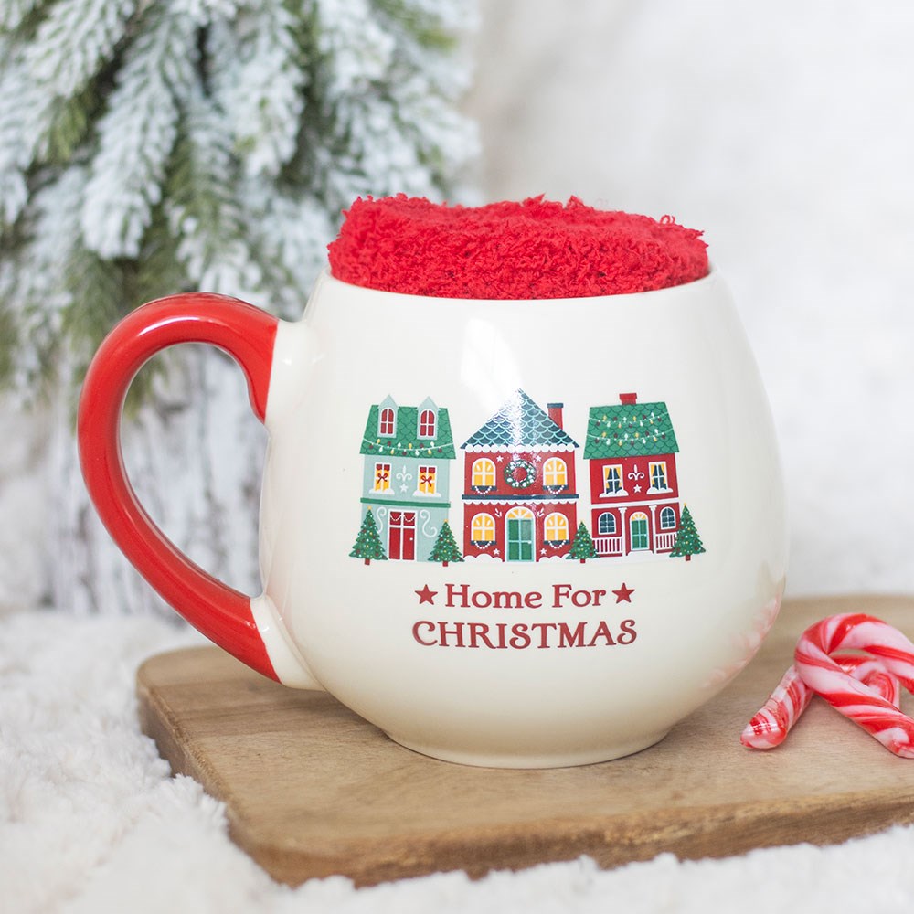 Cream ceramic mug printed with a Christmas village and Home for Christmas, with red socks rolled into the top