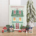 Twelve-day advent calendar shaped as a Christmas shopfront with small resin houses standing in front of it