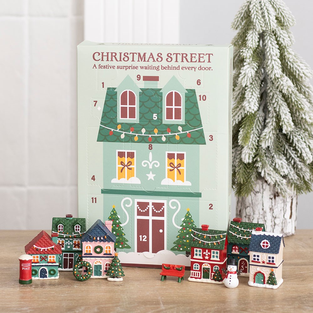 Twelve-day advent calendar shaped as a Christmas shopfront with small resin houses standing in front of it